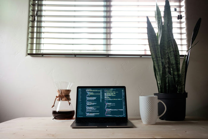 A laptop computer beside a cup of coffee on a desk in the morning
