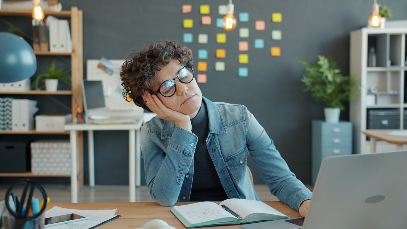 A tired person resting their head on their hand at a desk